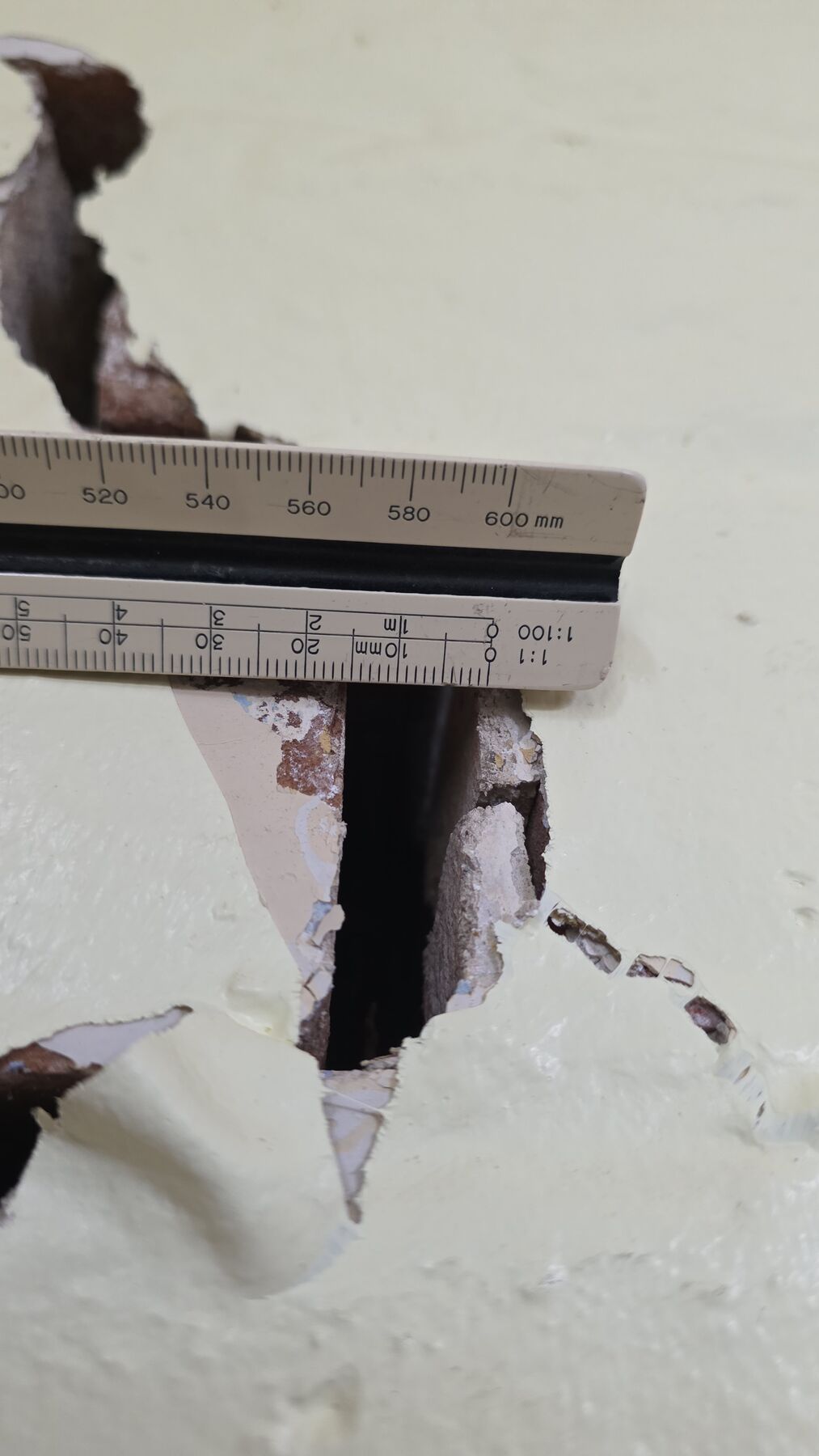 Crack width being measured with a rule against a cracked plastered wall